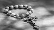 © Elmin - A rosary beads rest against a plain background. The photo is in black and white.