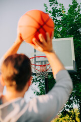 Wall Mural - A person prepares to shoot a basketball toward a hoop, with the focus on the ball and hoop in the background. The image captures the anticipation of the shot in a vibrant outdoor