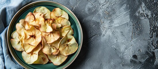 Poster - Healthy apple chips on a round green plate with a blue cotton kitchen towel on a grey background. with copy space image. Place for adding text or design