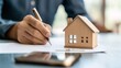 © Pojjanee - Signing the Deal: A close-up shot of a hand signing paperwork, with a miniature wooden house model nearby, symbolizing the commitment and excitement of a new home purchase.
