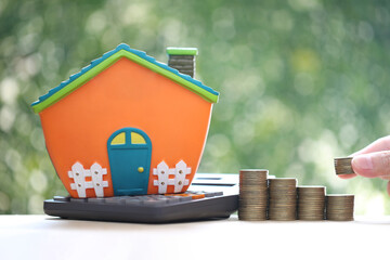 Poster - Calculating interest payments, Model house on calculator and stack of coins money on natural green background,Business investment and real estate concept