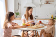 © sementsova321 - Young Caucasian smiling and cheerful mother sitting at the table in the kitchen with her cute daughters enjoying healthy breakfast together in their cozy home