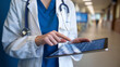 © ontsunan - Doctor using a digital tablet to access medical records in a hospital corridor, emphasizing technology in healthcare.
