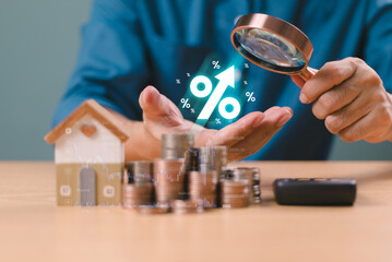 Interest rate financial, mortgage rates rise concept. Businessman use magnifying glass find percentage symbol, up arrow on coins stack with wooden home. Interest rate increase, high return tax fund.