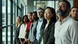© VK Studio - A line of professionals in a business setting, each exuding confidence and dedication, standing beside large windows that bathe them in natural light.