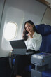 © Phimwilai - Confident successful Asian businesswoman sitting in airplane and working on laptop. Fly in first class In online business work in finance International business contacts business tourism.