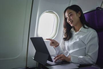 Confident successful Asian businesswoman sitting in airplane and working on laptop. Fly in first class In online business work in finance International business contacts business tourism.