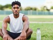 © Steveandfriend - Focused athlete sitting on grass, enjoying hydration with water bottle. Perfect for wellness and fitness themes.