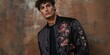 © Murda - Man in black floral bomber jacket against brown wall.