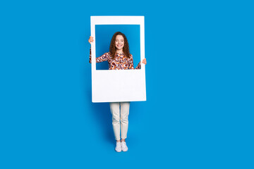 Full length photo of lovely young lady hold instant photo frame dressed stylish colorful garment isolated on blue color background