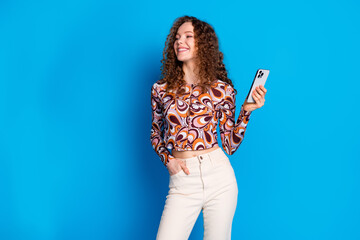 Wall Mural - Photo portrait of lovely young lady hold gadget look empty space dressed stylish colorful garment isolated on blue color background