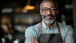 © svastix - A man wearing glasses and an apron stands confidently in a cafe, smiling warmly at the camera, reflecting warmth and expertise in his craft, creating a genuine connection.