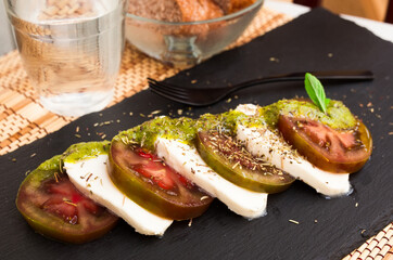 Wall Mural - Caprese salad with mozzarella, black tomatoes and pesto on black stone plate