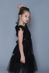 A young girl in a black ruffled dress poses playfully with her arms raised, showing a fun and lighthearted moment. This image captures the blend of elegance and youthful spirit in children's fashion.