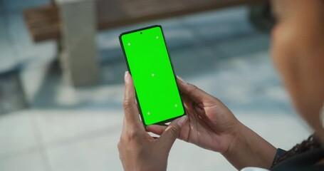Female Hand Holding a Smartphone with Green Screen Mock Up Display. Black Woman is Standing on a Street and Checking Content on a Mobile Device. Close Up Over the Shoulder Footage