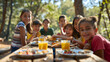 © Gita - A group of children gathered at a wooden picnic table in a sunny forest, smiling and enjoying a meal with drinks and healthy food, bonding in nature.