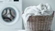 © svastix - A wicker basket filled with freshly washed and neatly folded white towels sitting next to a washing machine, representing cleanliness and household chores in a serene setting.