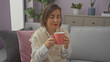 © Krakenimages.com - Middle-aged woman enjoying a cup of tea on a cozy couch in a modern living room setting.