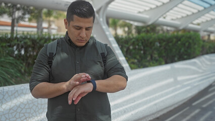 A young hispanic man checks his watch on a city street, evoking themes of punctuality, urban lifestyle, and modern technology.