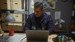 © Krakenimages.com - A focused hispanic man wearing a police uniform works intently at his laptop in a well-equipped detective's office.