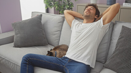 Poster - Young hispanic man relaxing at home with a pet cat on a cozy couch in a well-lit room.