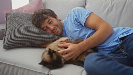 Poster - A smiling man cuddles with a siamese cat on a couch in a cozy living room setting