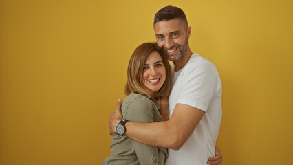 Man and woman smiling together in a loving embrace against a vibrant yellow wall, showcasing their happy relationship and closeness