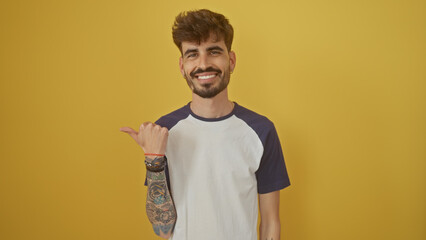 Poster - Handsome young man with beard smiling and pointing left over isolated yellow background