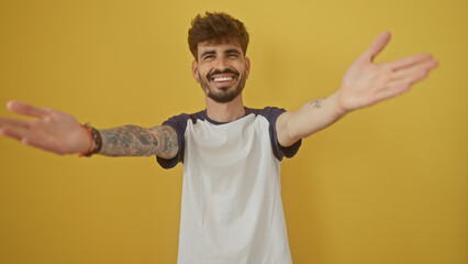 Poster - A smiling young hispanic man with a beard and tattoos stretching his arms for a hug against a yellow background.