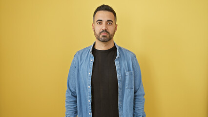 Wall Mural - Handsome hispanic man with beard in denim jacket against yellow background