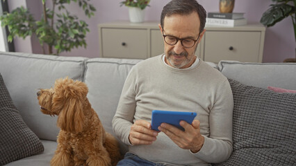 Sticker - A middle-aged man relaxes with his poodle on a couch at home, looking at a tablet