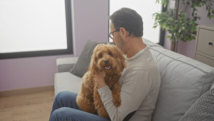 Canvas Print - Middle-aged hispanic man smiling at his poodle inside a cozy apartment living room.