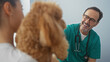 © Krakenimages.com - A smiling hispanic man in scrubs interacts with a poodle in a veterinary clinic setting, indicating professional pet care.