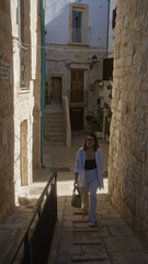 Wall Mural - A young, beautiful, hispanic woman walks the historic stone streets of polignano a mare, puglia, italy, basking in the charming european architecture.