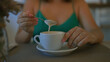© Krakenimages.com - A young hispanic woman enjoying coffee in an italian cafeteria, gently stirring the froth with a spoon indoors.