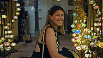 Smiling young woman enjoying traditional souk at souk madinat jumeirah in dubai, surrounded by colorful lanterns.