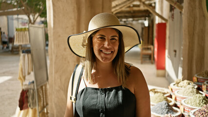 Smiling woman wearing sunhat explores traditional souq market in dubai.