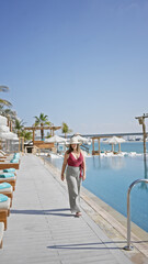 Poster - A stylish woman walks by a luxurious infinity pool at a resort, embodying leisure and elegance.