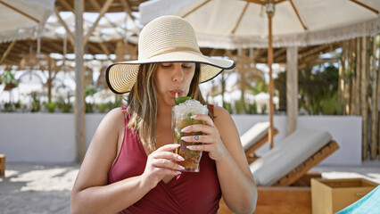 Wall Mural - A young woman in a sunhat sipping a mojito at a luxurious beach resort.