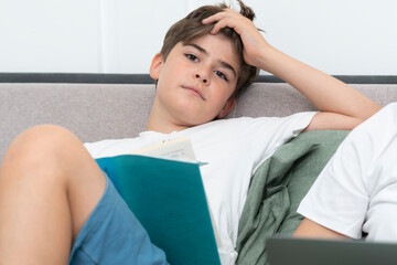 Tired school boy reading book in the bedroom