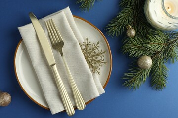 Poster - Beautiful Christmas setting with plate, elegant cutlery and festive decor on blue table, flat lay