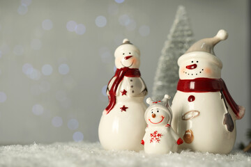 Wall Mural - Cute decorative snowmen on artificial snow against blurred lights. Space for text