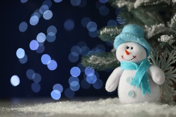 Wall Mural - Cute decorative snowman and fir branches on artificial snow against blurred lights. Space for text