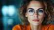 © svastix - A young woman with curly hair and glasses, staring intently at the camera, presenting a confident and assertive look, with a blurred background highlighting her focus.