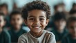 © svastix - A young boy smiles confidently while sitting in a classroom, with his classmates and classroom furniture blurred in the background, representing education and childhood joy.