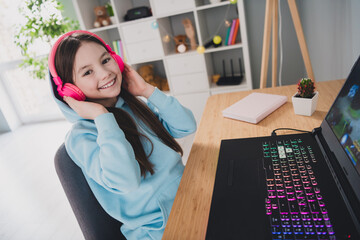 Wall Mural - Photo of cheerful cute girl little gamer using modern technology enjoying melody computer indoors house