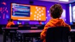 © PrusarooYakk - Young students in a classroom learning to code, with a focus on a boy in an orange hoodie looking at a brightly colored screen displaying code.