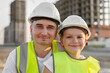 © Studio Peace - Portrait of a positive father and son in protective helmets on the background of a construction site