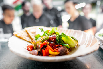 Wall Mural - close-up of vibrant, gourmet dish featuring grilled vegetables and greens, served on elegant plate with blurred restaurant background. Perfect for culinary, fine dining, and food photography themes.