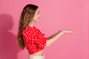 Wall Mural - Photo portrait of lovely teen lady profile hold empty space dressed stylish red garment isolated on pink color background